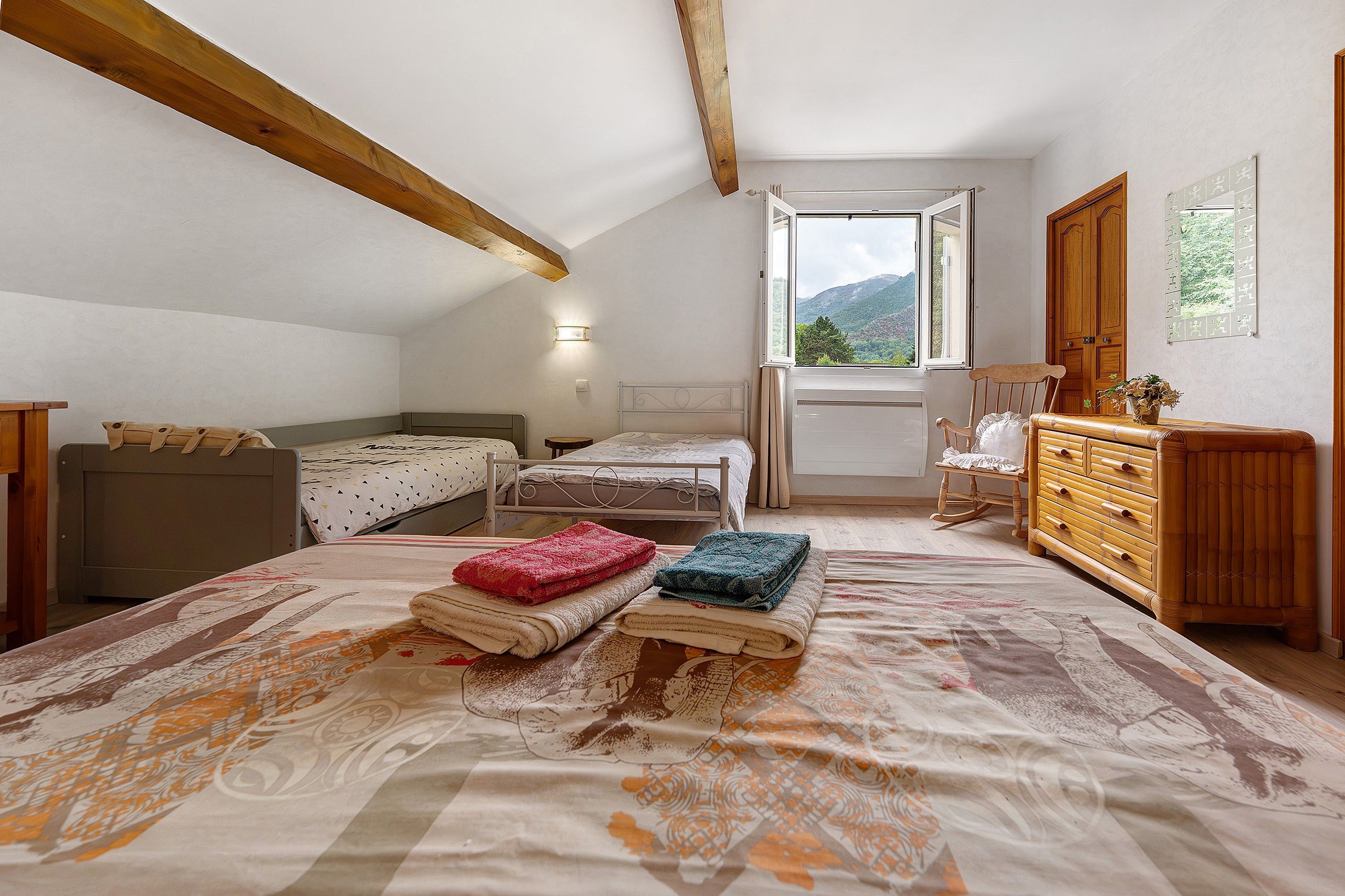 Un dormitorio con dos camas individuales, un aparador de madera, una mecedora y una ventana con vistas a la montaña.