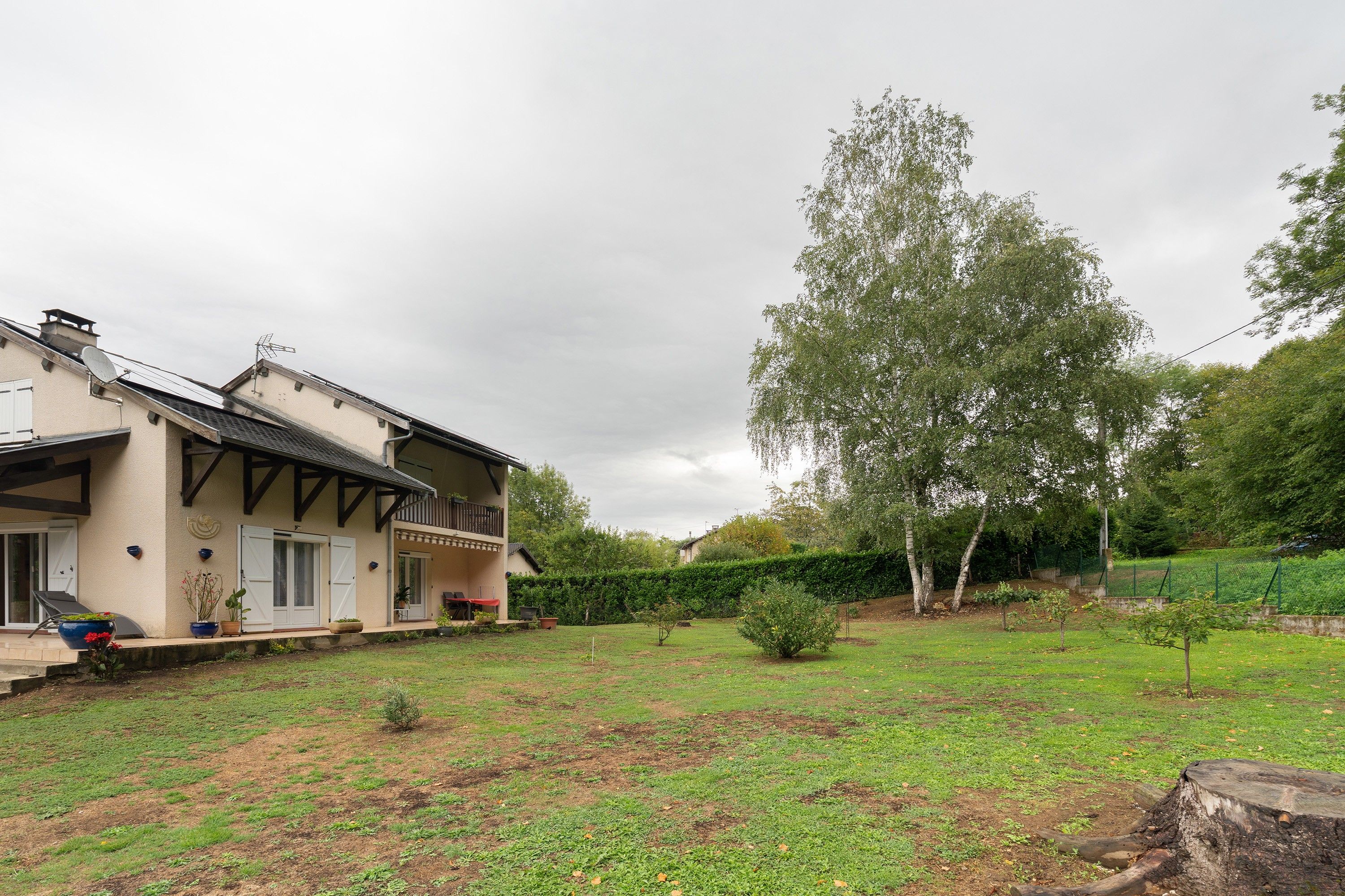 A two-story house with a balcony, a garden, and a large tree.