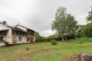 A two-story house with a balcony, a garden, and a large tree.
