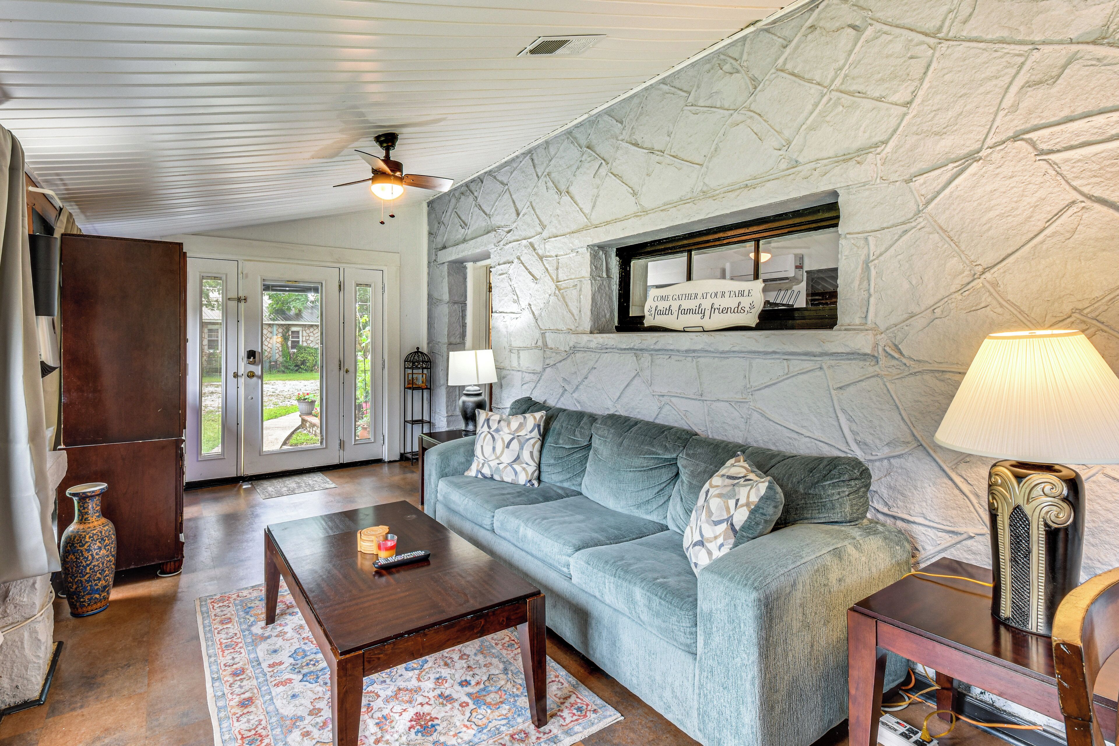 A living room with a stone wall, a sofa, a coffee table, a lamp, and a sign on the wall.