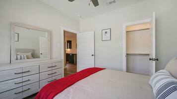 A bedroom with a bed, a dresser, a mirror, a closet, and a ceiling fan.