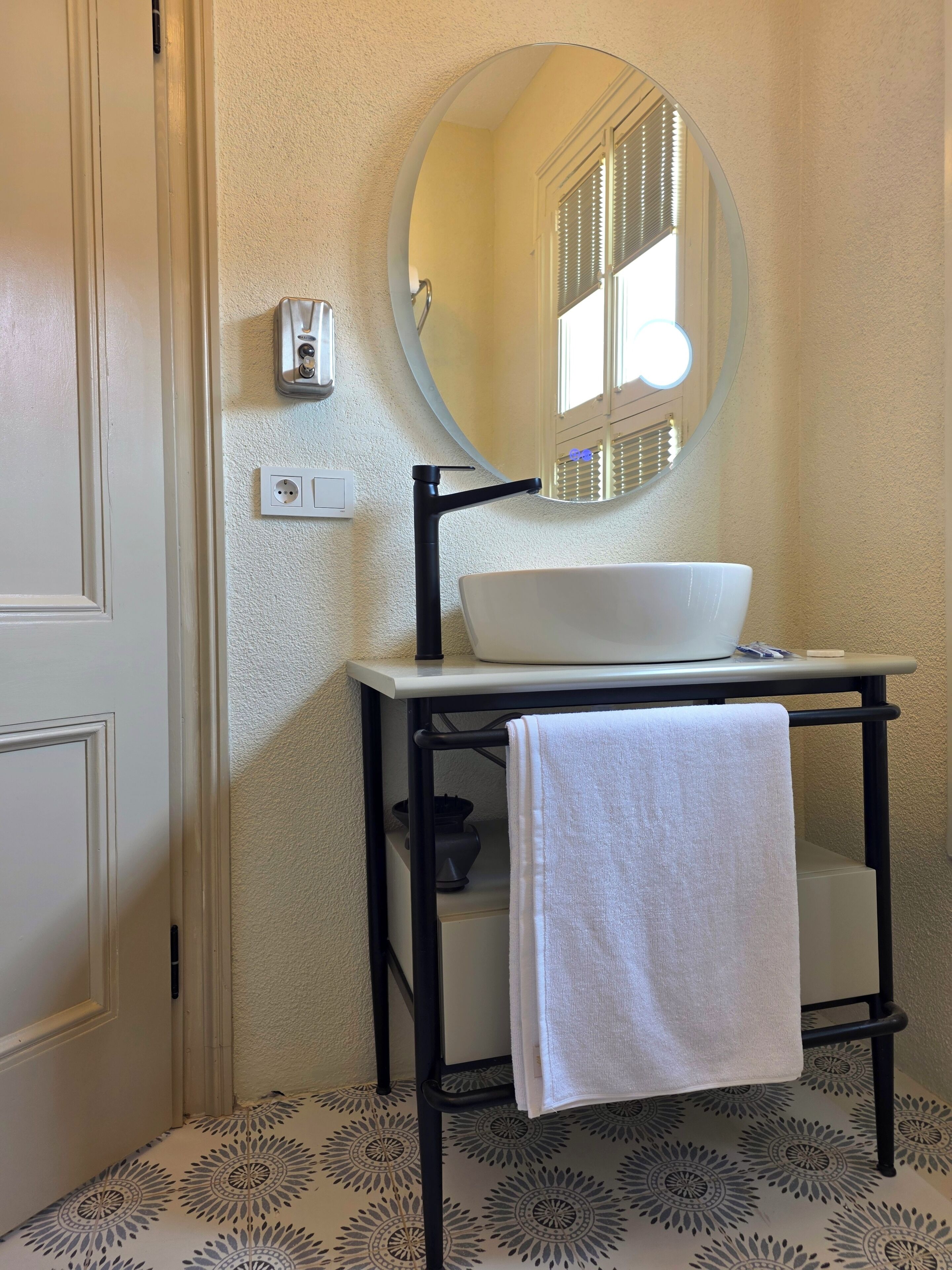 A bathroom with a white sink, a round mirror, and a towel hanging on a rack.