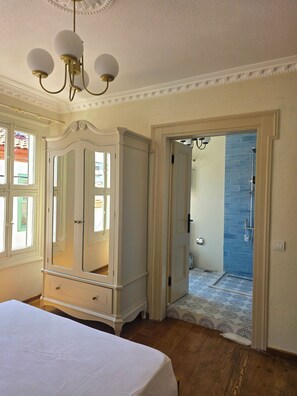 A bedroom with a large bed, a wardrobe, and a door leading to a bathroom with a blue tiled wall.