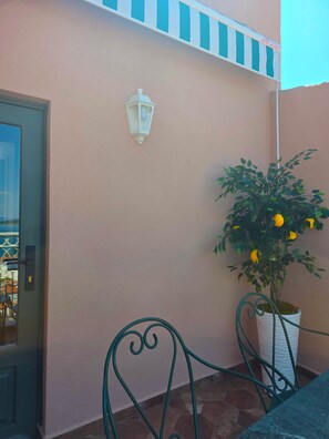 A room with a door, a wall-mounted light fixture, a potted plant with yellow fruit, and a metal chair. - Historic Greek House with Sea View in Ayvalik (Balıkesir)