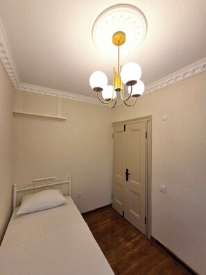 Ein Schlafzimmer mit einem Einzelbett, Holzboden, weißer Tür und einer Deckenleuchte.