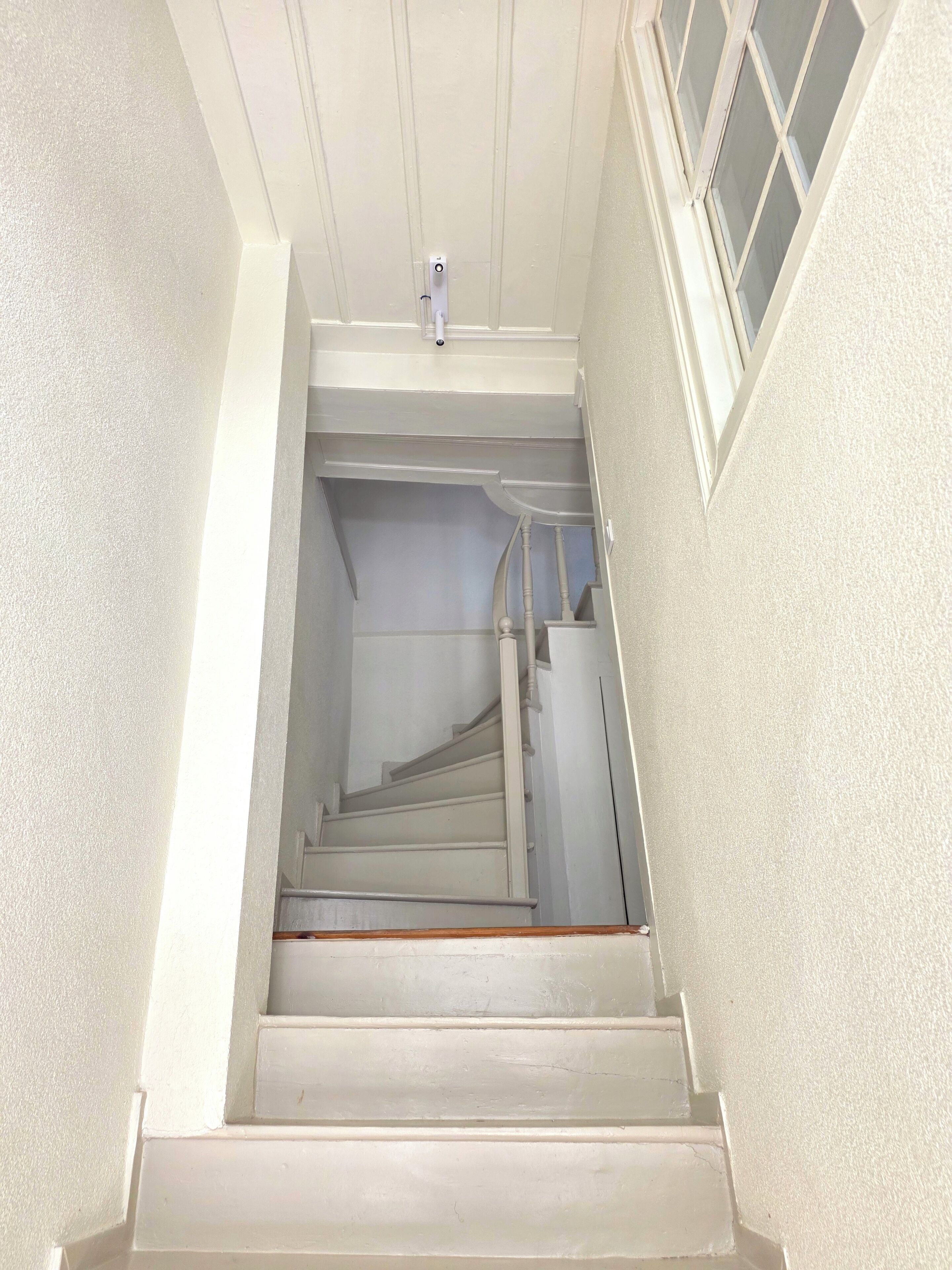 Un escalier avec une rampe, un interrupteur et une fenêtre à motifs géométriques.