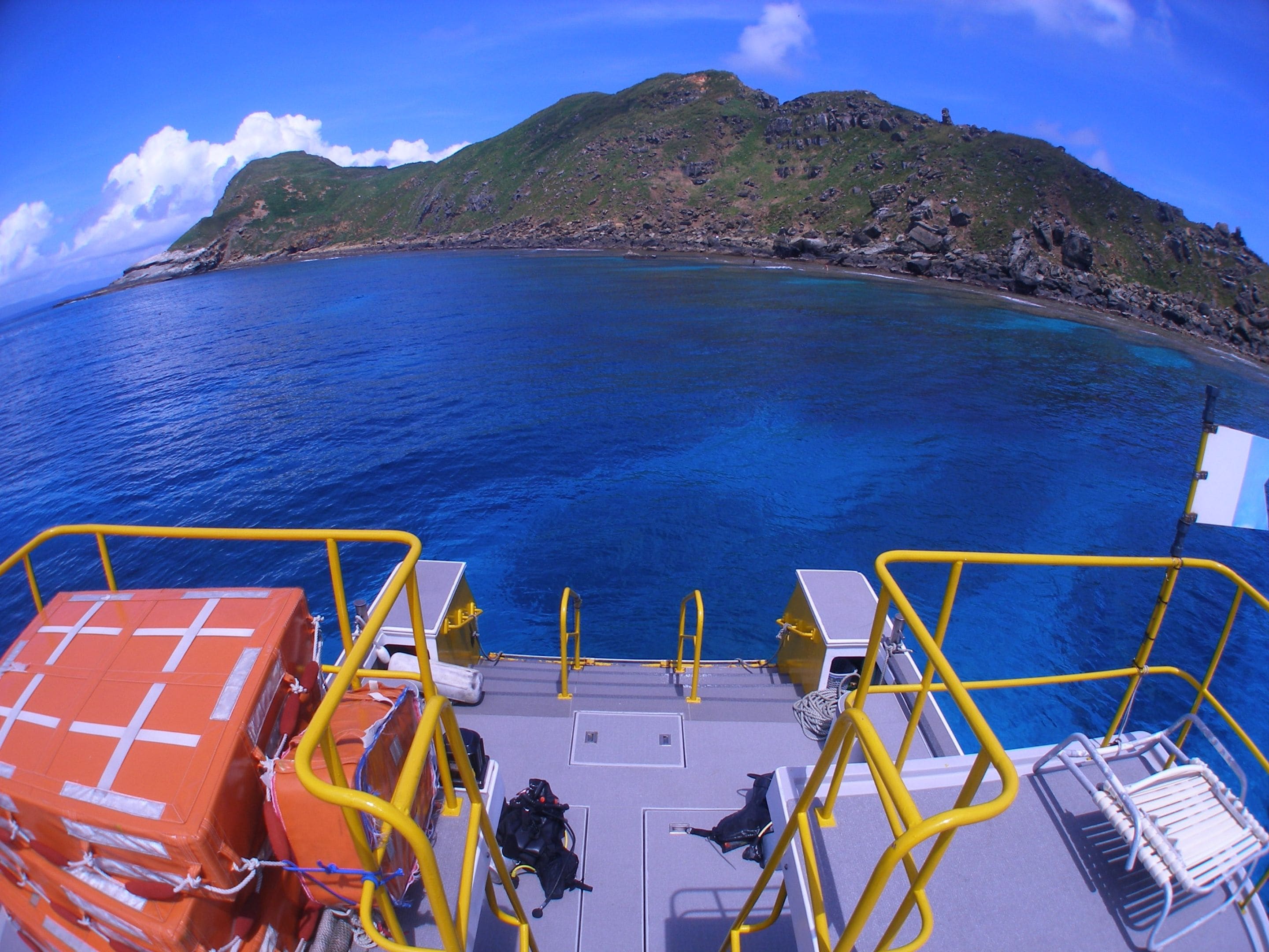 A boat deck with yellow railings, a lifeboat, and a view of a mountainous coastline.