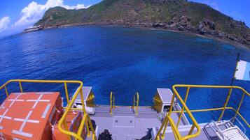 A boat deck with yellow railings, a lifeboat, and a view of a mountainous coastline.