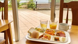 A tray with a sandwich, pasta, and a drink, placed on a table with a view of a body of water and mountains.