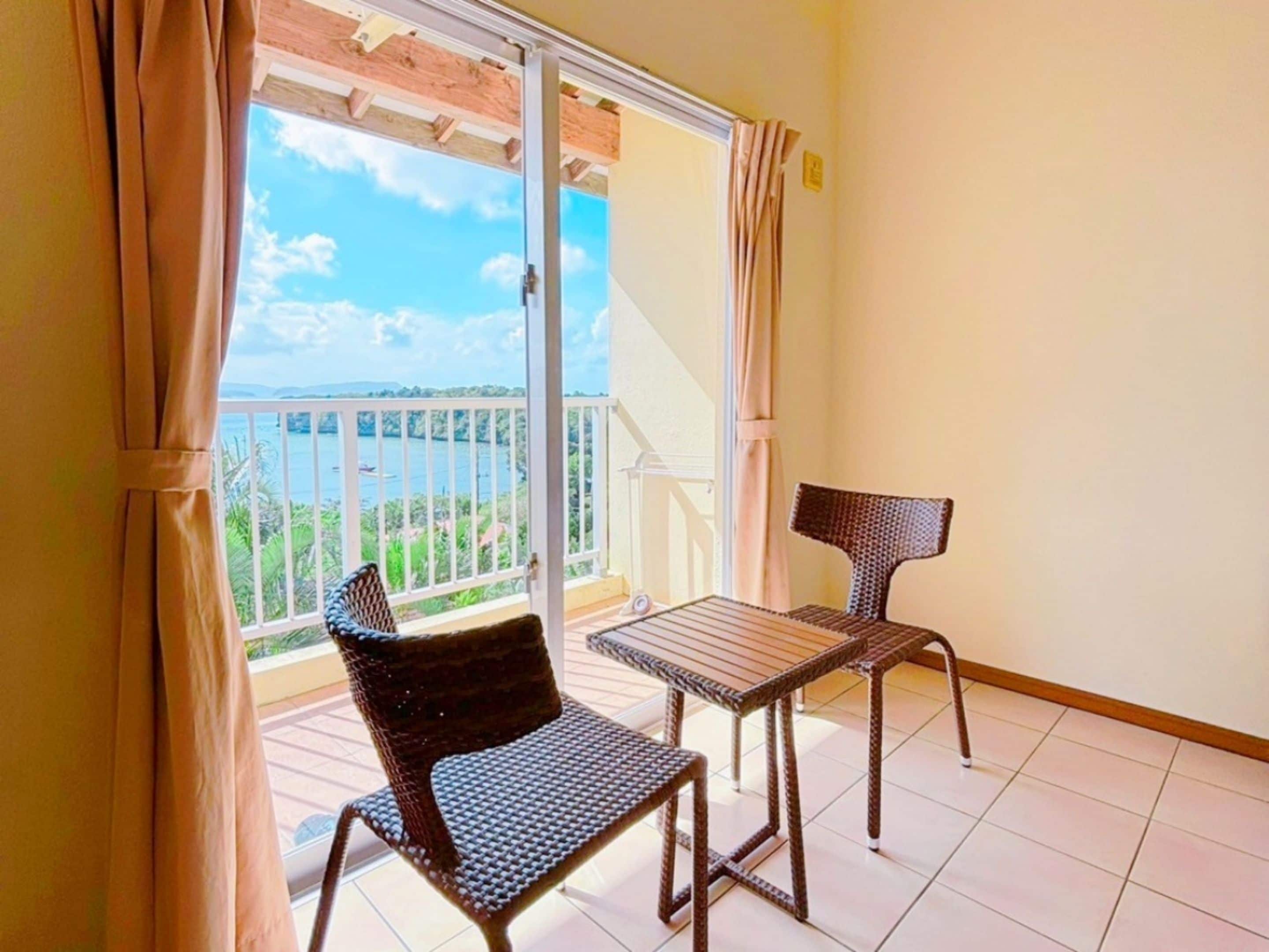 A balcony with a view of a body of water, two wicker chairs, and a small table.