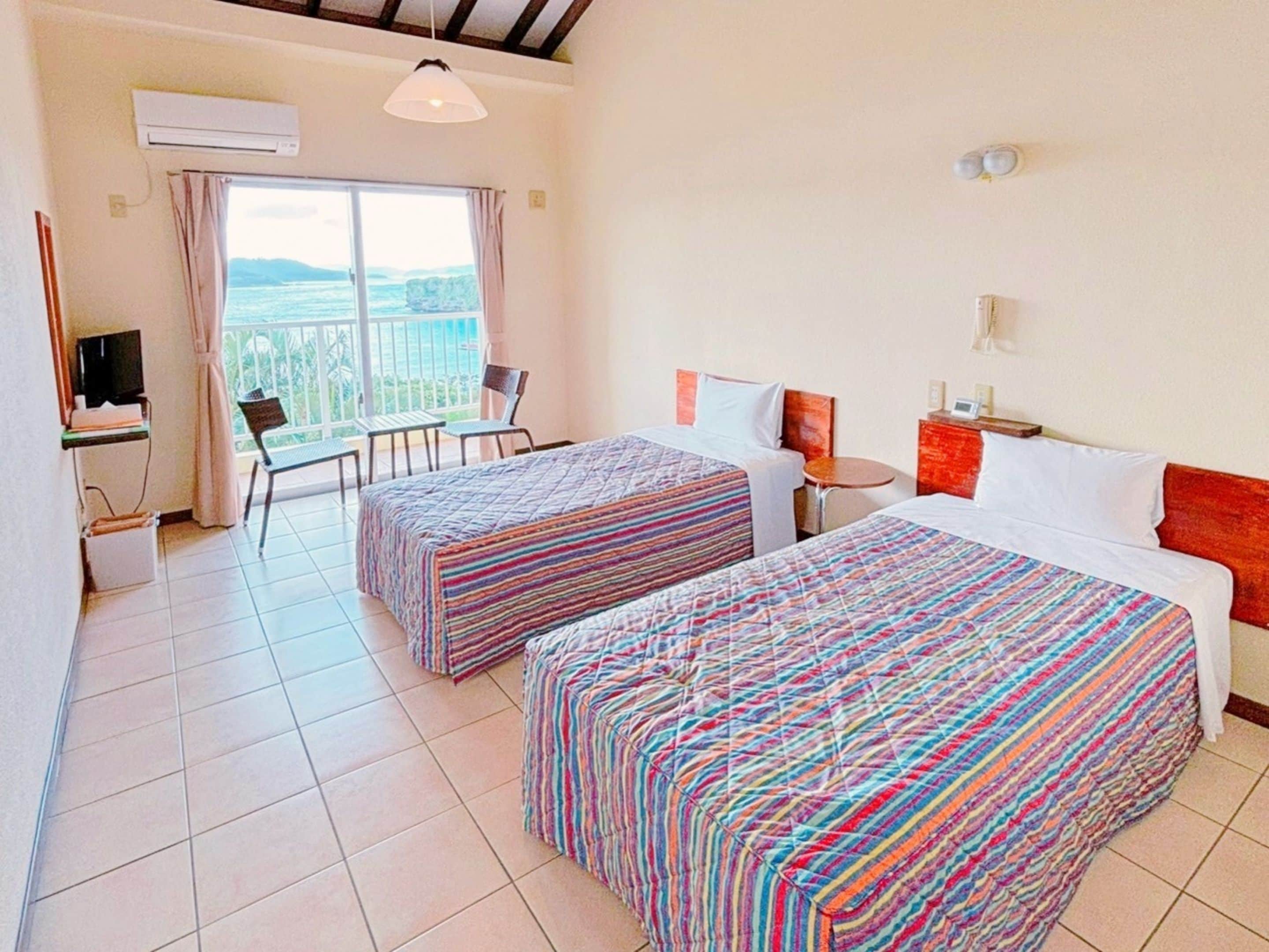 A hotel room with two beds, a desk with a computer, a chair, a small table, and a window with a view.