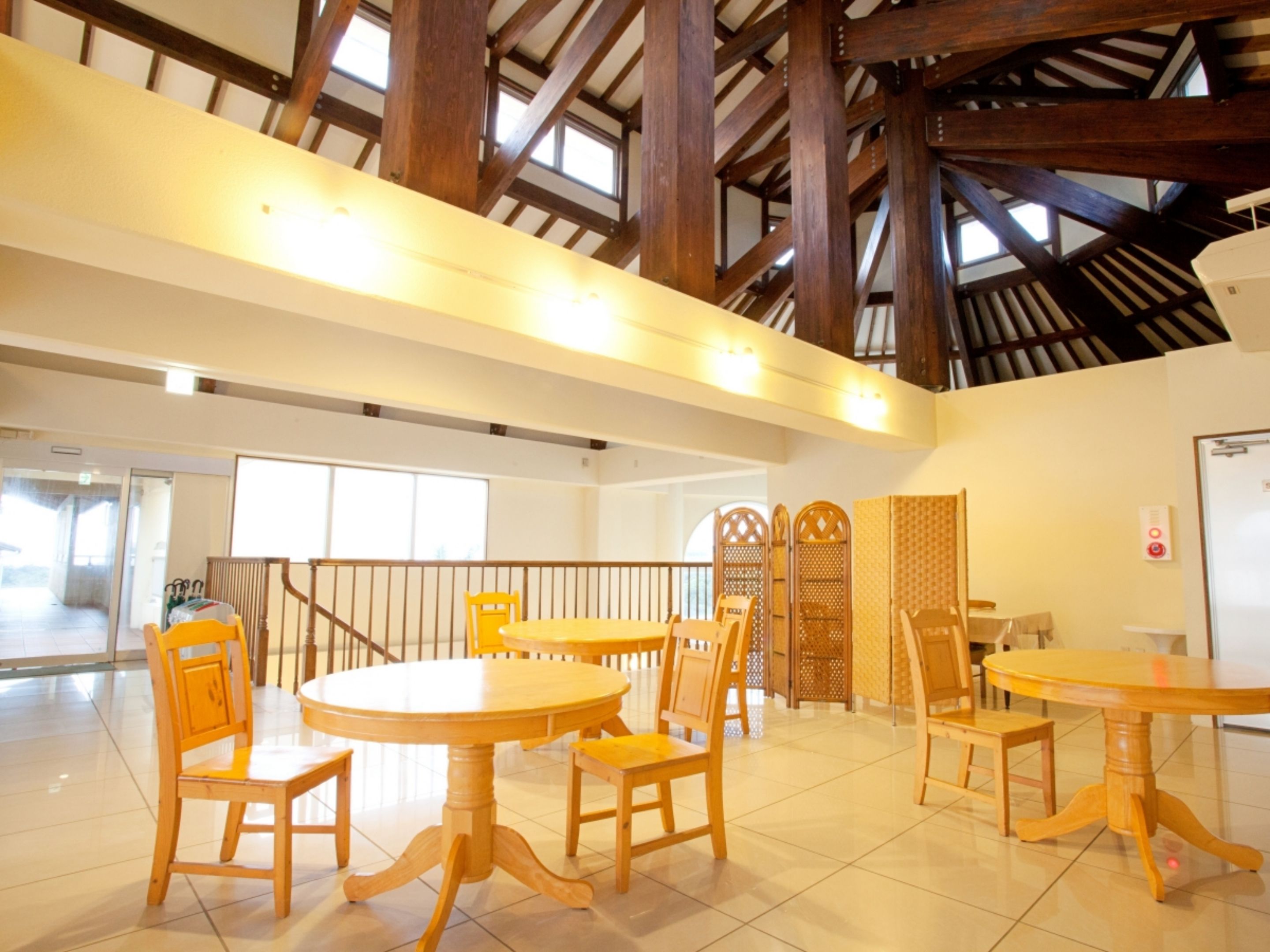 A spacious indoor area with high ceilings and wooden beams, featuring multiple round tables and chairs.