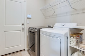 A laundry room with a front-loading washer and dryer, a drying rack, and a shelf with storage containers.