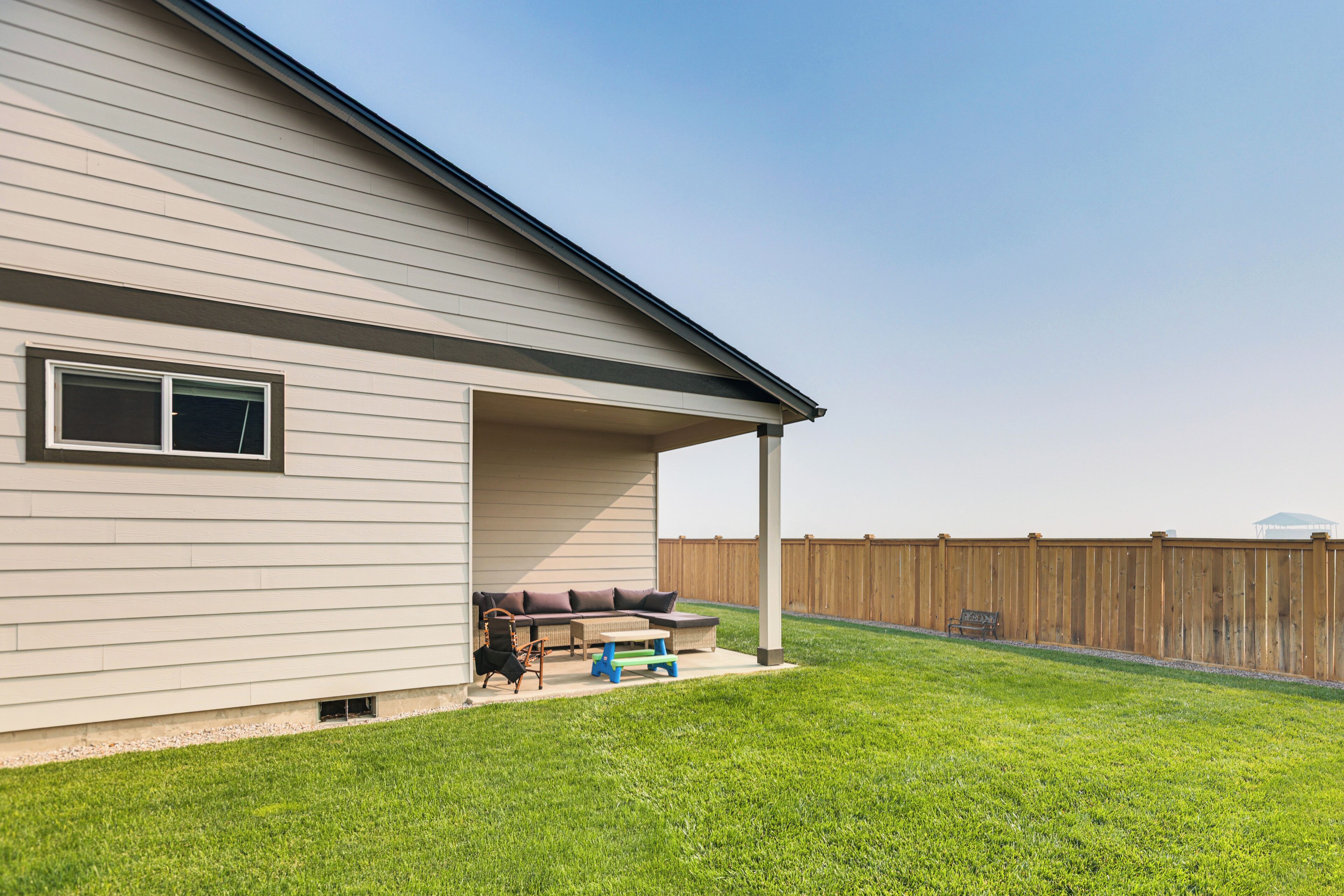 A house with a covered patio area, a lawn, and a wooden fence.