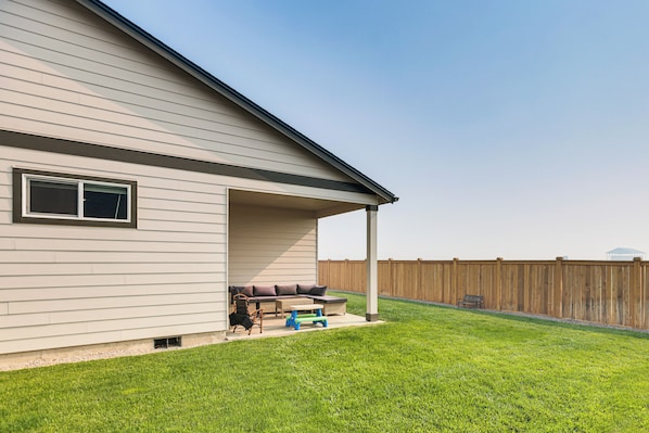 A house with a covered patio area, a lawn, and a wooden fence.