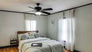 A bedroom with a bed, a ceiling fan, a nightstand, and a window with curtains.