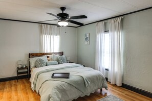 A bedroom with a bed, a ceiling fan, a nightstand, and a window with curtains.