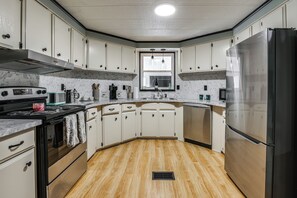 Una cocina con armarios blancos, un refrigerador de acero inoxidable, una estufa y una ventana sobre el fregadero.