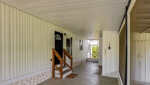 A corridor with a stone wall, wooden staircase, and a door leading to a covered area.