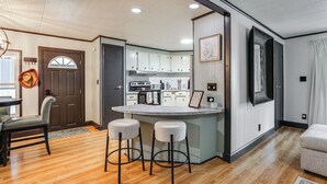 A modern kitchen with white cabinets, a central island with stools, and a dining area with a wooden table and chairs.