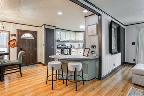 A modern kitchen with white cabinets, a central island with stools, and a dining area with a wooden table and chairs.