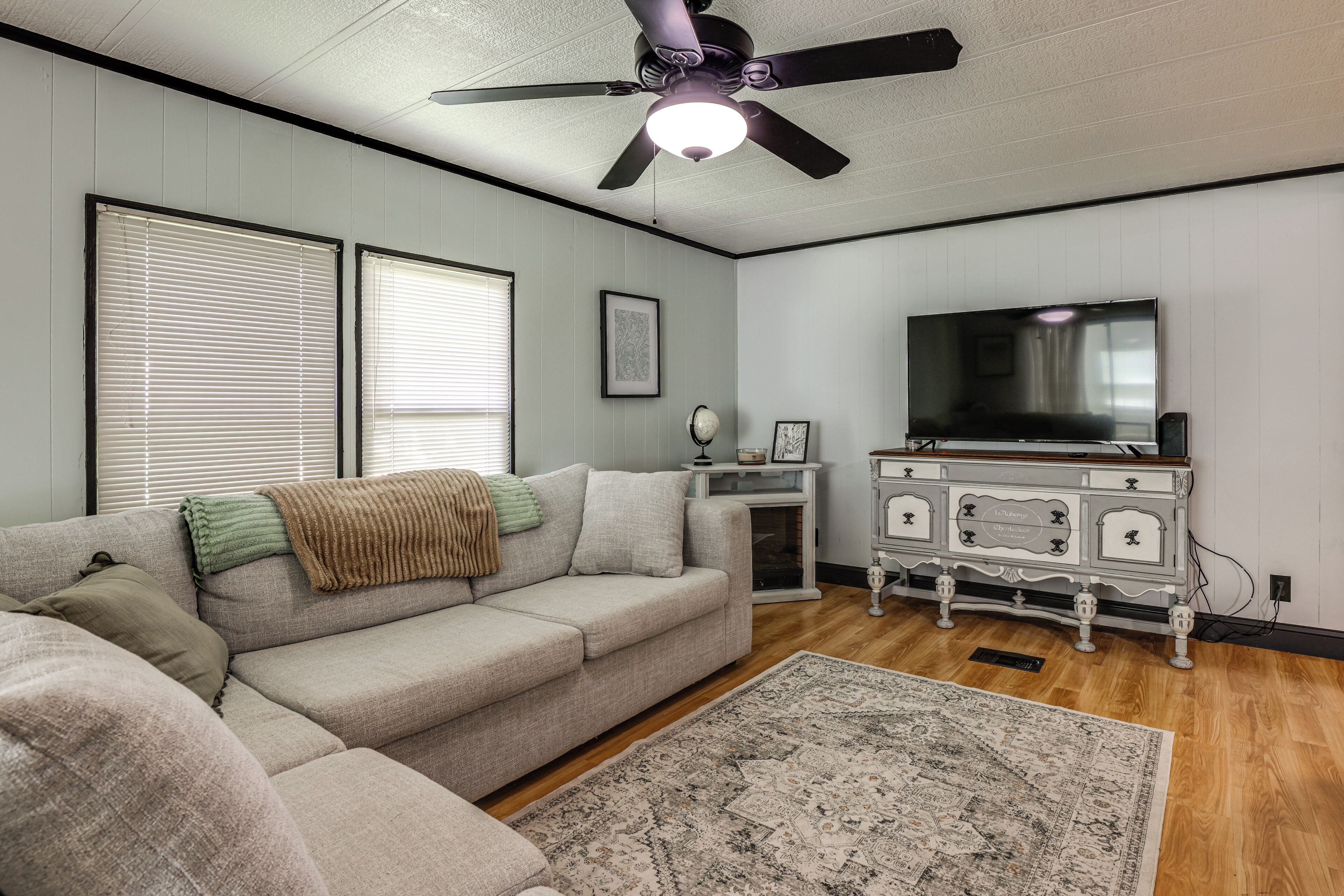 A living room with a sectional sofa, a flat-screen TV, a ceiling fan, and a decorative cabinet.