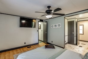 Un dormitorio con cama, ventilador de techo, televisor de pantalla plana, una puerta y un cuadro de peces en la pared.