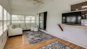 A living room with a white sofa, a television mounted on the wall, and a ceiling fan.