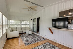 A living room with a white sofa, a television mounted on the wall, and a ceiling fan.