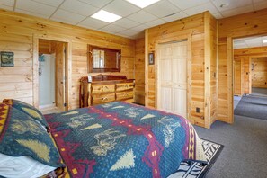 Una habitación de cabaña de madera con una cama, tocador y una puerta que da a otra habitación.