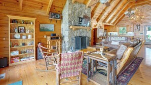 A cozy log cabin interior with a stone fireplace, wooden furniture, and a bookshelf filled with books and games. - Mountain Top Lodge with Amazing Vista (Jasper)