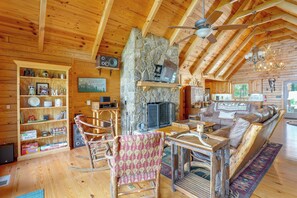 A cozy log cabin interior with a stone fireplace, wooden furniture, and a bookshelf filled with books and games. - Mountain Top Lodge with Amazing Vista (Jasper)