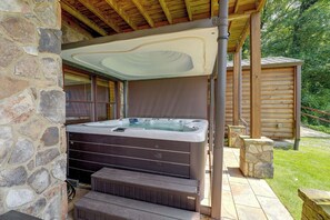 Fachada de piedra con terraza de madera, jacuzzi y zona cubierta con techo de madera.