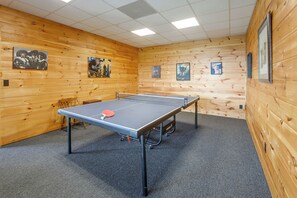Una mesa de ping pong en una habitación con paredes y techo de madera, suelo alfombrado y cuadros enmarcados en las paredes.