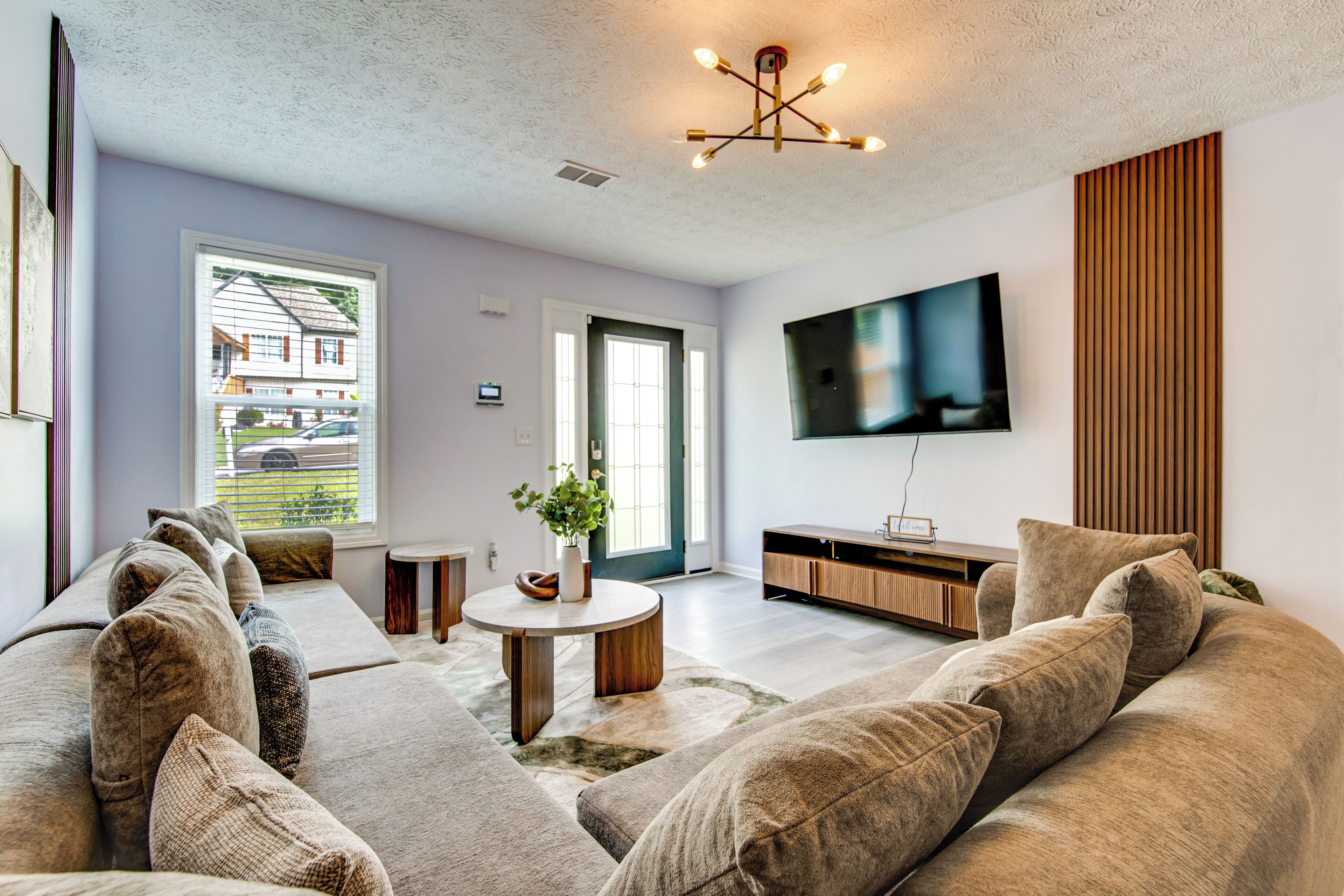A modern living room with a sectional sofa, a round coffee table, and a flat-screen TV mounted on the wall.