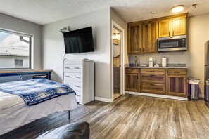 A bedroom with a bed, a dresser, and a television. There is a kitchenette with a microwave and cabinets. - Golf, Fish & Explore: Updated Unit in Oakland City (Oakland City)