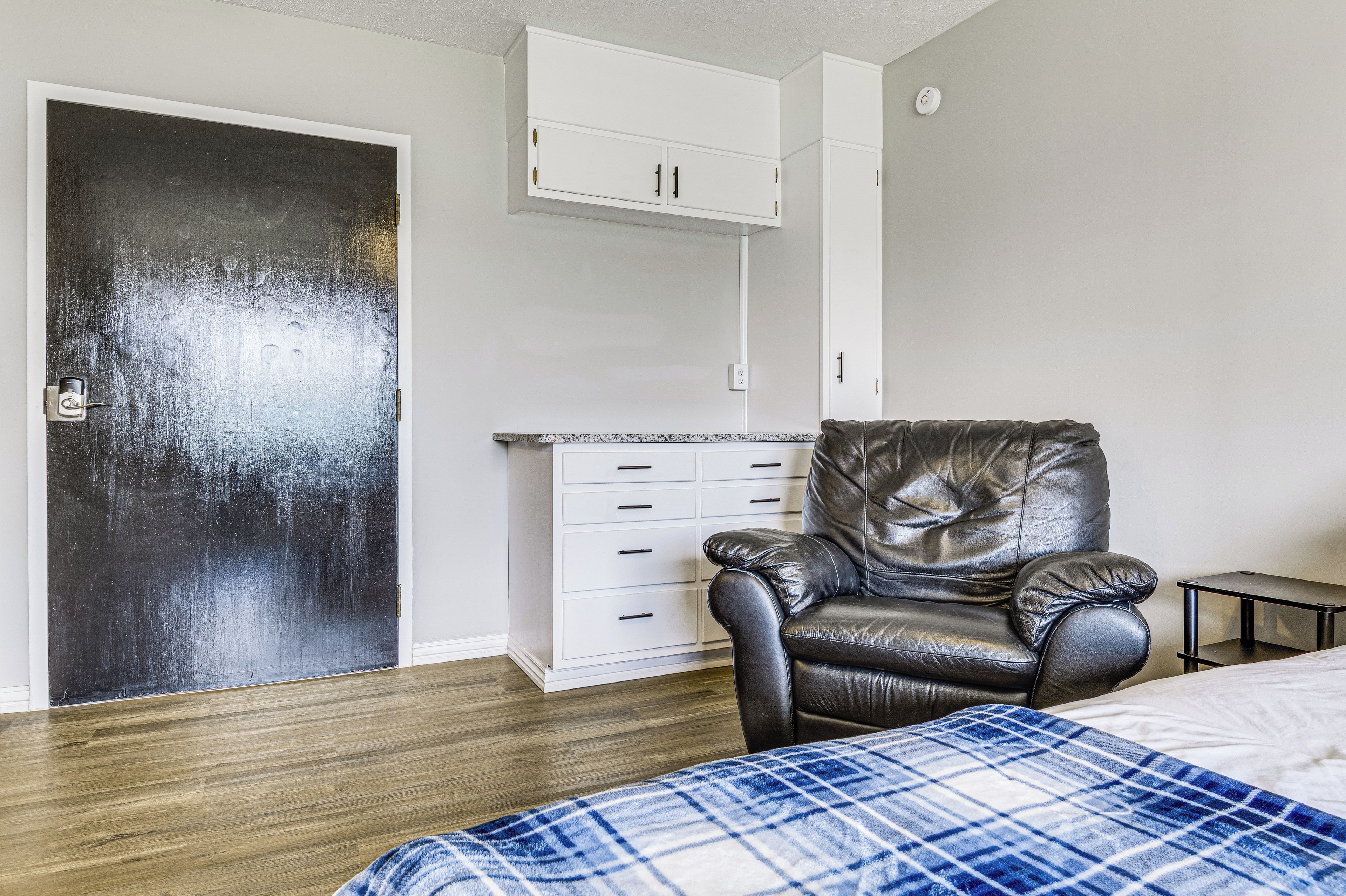 A room with a bed, a leather chair, a white cabinet, and a door.
