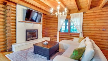 A log cabin interior with a fireplace, television, and a sofa.