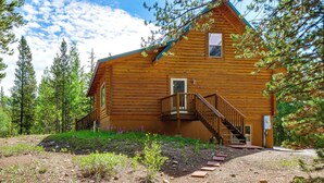 A log cabin with a wooden staircase leading to a deck, surrounded by trees and a gravel path. - Pool Table & Peaceful Porch: Fairplay Retreat (Fairplay)
