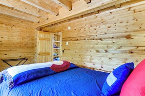 Ein Holzhüttenraum mit einem Bett, einem Bücherregal und einer Tür zu einem weiteren Raum.