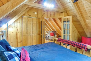 Ein Zimmer mit hohen Holzbalken, einem Bett, einem Sessel und einem Tisch.