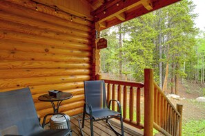 Eine Holz-Blockhütte mit Veranda, zwei Stühlen, einem kleinen Tisch und einem Schild mit der Aufschrift 'The Porch Sit & Relax'.