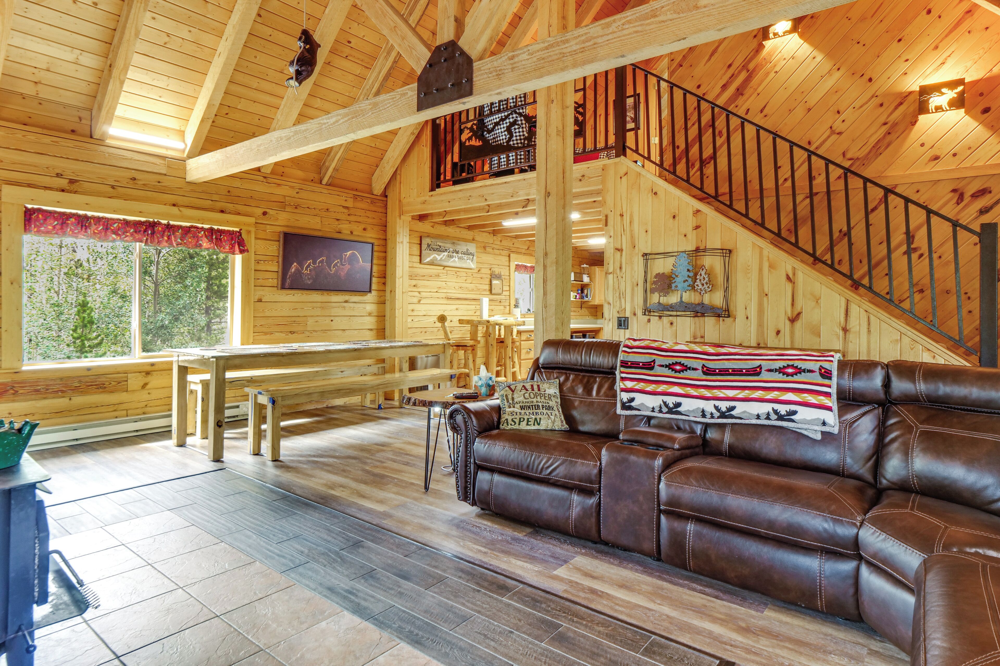 A log cabin interior with a wooden staircase, leather sofa, and a view of the outdoors.