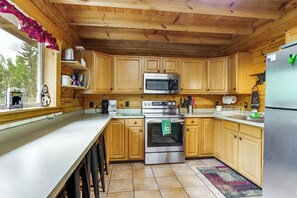 A kitchen with wooden cabinets, stainless steel appliances, and a window with a view of trees. - Pool Table & Peaceful Porch: Fairplay Retreat (Fairplay)