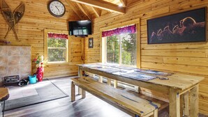 A wooden cabin interior with a wooden table, benches, a clock, a television, and windows with curtains. - Pool Table & Peaceful Porch: Fairplay Retreat (Fairplay)