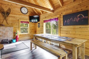 Ein Holzhäuschen im Inneren mit einem Holztisch, Bänken, einer Uhr, einem Fernseher und Fenstern mit Vorhängen.