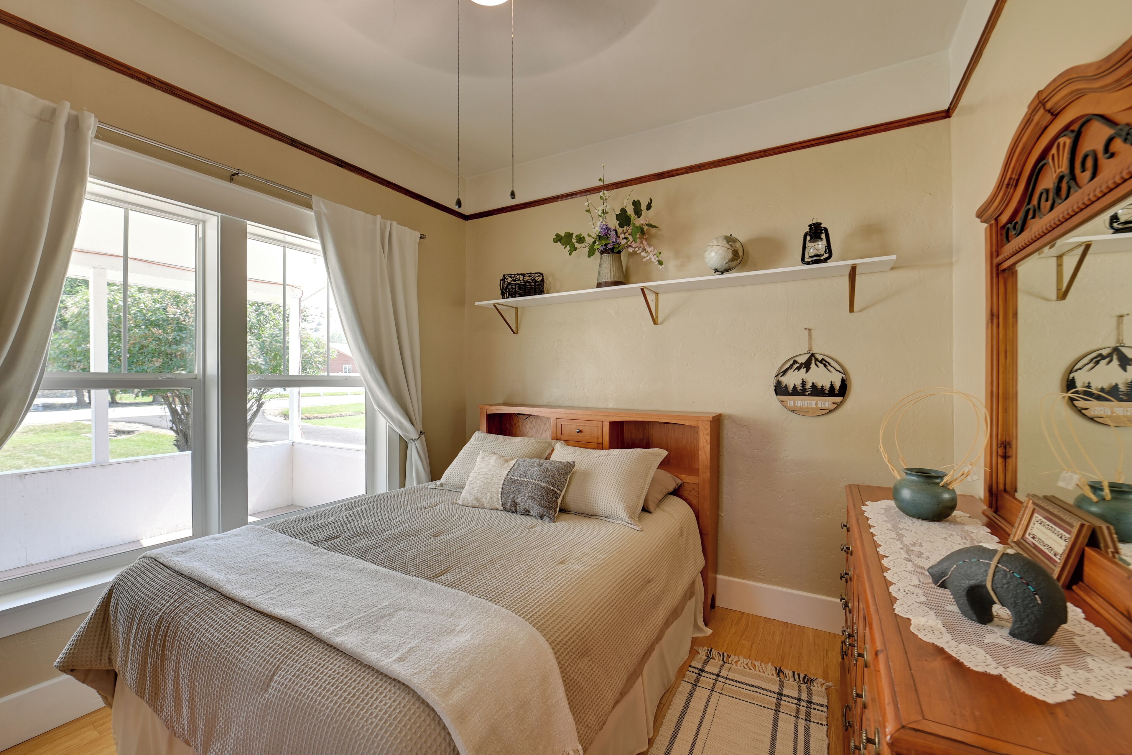 Une chambre à coucher avec un grand lit, une commode en bois, un miroir et une fenêtre avec des rideaux.