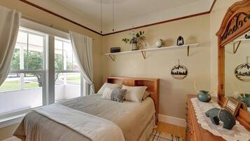 Une chambre à coucher avec un grand lit, une commode en bois, un miroir et une fenêtre avec des rideaux.