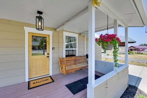 A porch with a wooden bench, a welcome mat, and a hanging flower basket.