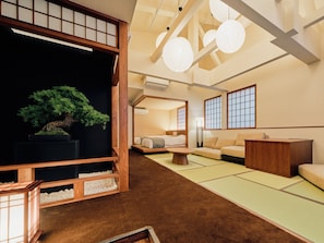 A traditional Japanese-style room with tatami flooring, a low wooden bed, a tatami mat table, and a bonsai tree.